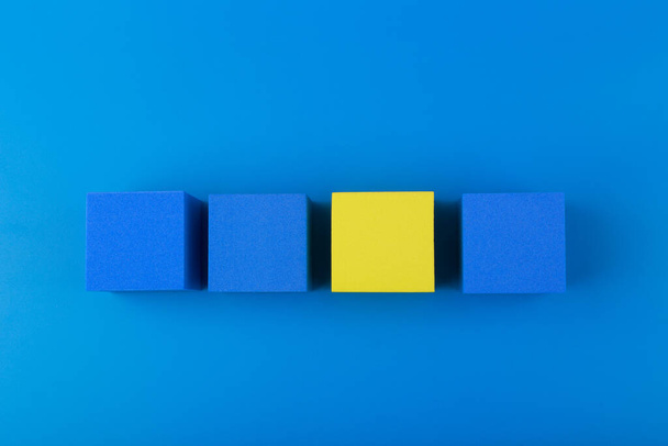 Widok z góry trzy niebieskie i jeden żółty bloki na niebieskim tle. Pojęcie indywidualności - Zdjęcie, obraz
