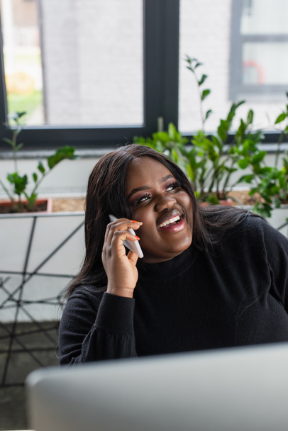 happy african american plus size businesswoman talking on smartphone in office  - Photo, Image