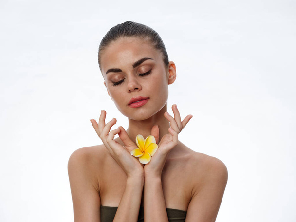 portrait of a beautiful woman with closed eyes and a yellow flower in her hands on a light background - Photo, Image