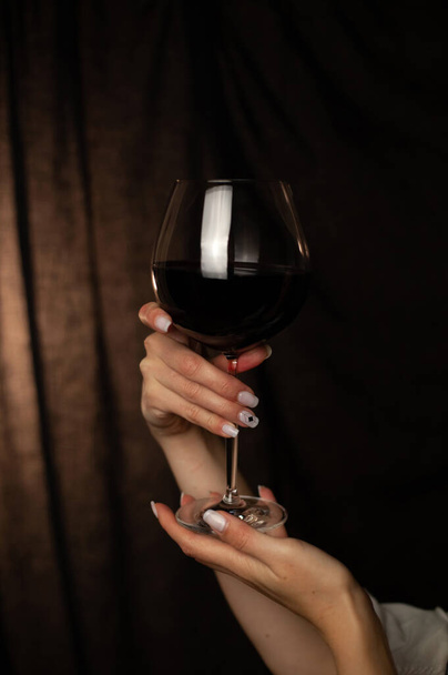 A beautiful, large glass with red wine in the hands of the girl. Dark background and selective focus - Φωτογραφία, εικόνα