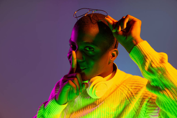 Portrait de jeune homme africain beau posant isolé sur fond de studio sous la lumière du néon dégradé - Photo, image