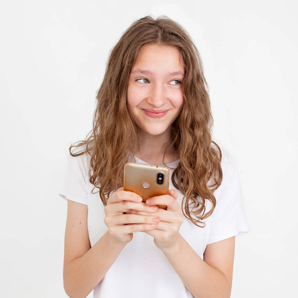 Surprised young girl using mobile phone with positive expression, smiles broadly, dressed in casual clothing and standing isolated on white background. People lifestyle concept. Happy Teen Using mobile phone typing sms message Looks away - Foto, imagen