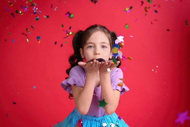 Adorable little girl blowing confetti on red background - Photo, Image