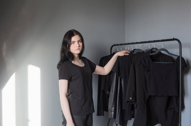 teen girl in black jeans and a t-shirt near  hanger with black clothes - Fotografie, Obrázek
