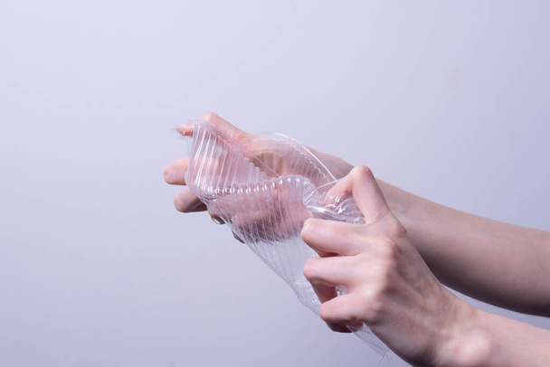 la mano femenina arruga el embalaje plástico transparente sobre fondo gris - Foto, Imagen