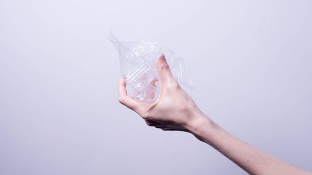 γυναικείο χέρι τσαλακώνει διαφανή πλαστική συσκευασία σε γκρι φόντο - Φωτογραφία, εικόνα