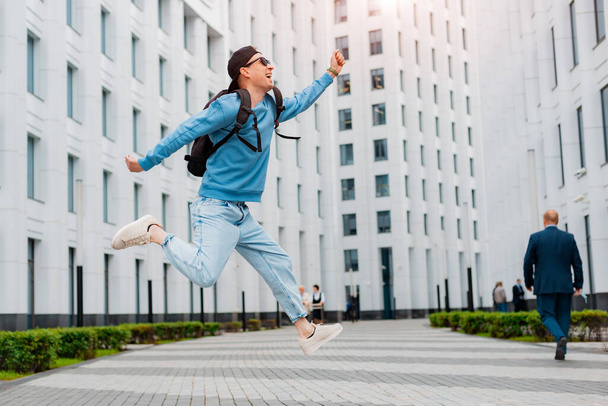 joven chico con estilo en la ropa azul salta en el fondo de un edificio moderno blanco. - Foto, Imagen