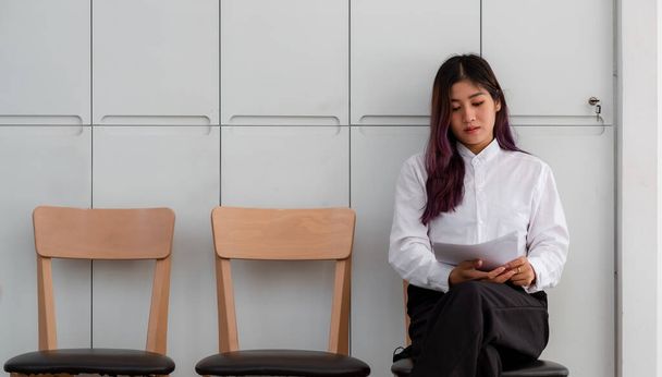 Ázsiai nő önéletrajzzal ül, hogy vizsgálja felül a dokumentumokat, miközben várja az állásinterjút - Fotó, kép