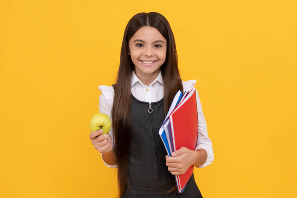 Szczęśliwy dzieciak z powrotem do szkoły gospodarstwa jabłko i książki żółte tło, 1 września - Zdjęcie, obraz