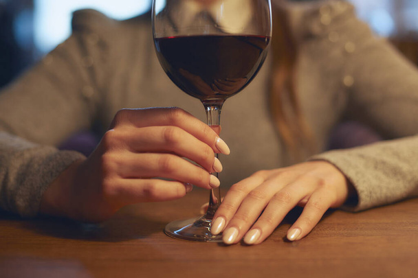 Hand of a young beautiful girl holding a glass of wine indoors of a stylish wine restaurant - Foto, afbeelding