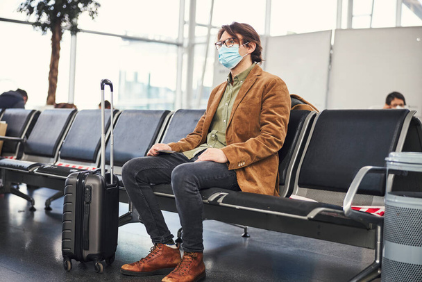 Jeune homme en masque médical en attente du vol à l'aéroport - Photo, image