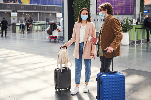 Мужчина и женщина в медицинских масках стоят в терминале аэропорта - Фото, изображение