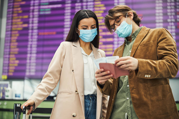Мужчина и женщина в медицинских масках проверяют билеты в аэропорту - Фото, изображение