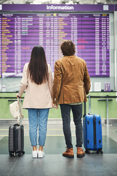 Jóvenes viajeros en pareja mirando a bordo de salida en el aeropuerto - Foto, Imagen