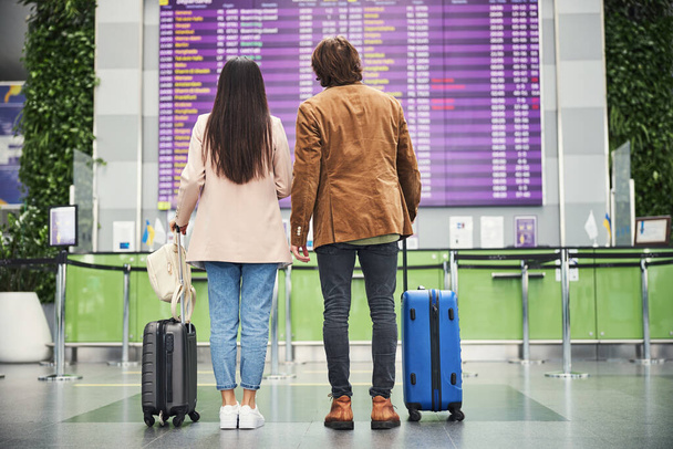 Young couple travelers checking time of plane arrival at airport - 写真・画像