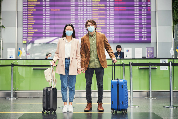 Молода пара мандрівників у медичних масках, що стоять в аеропорту
 - Фото, зображення