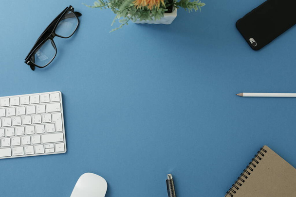 Очки клавиатуры цветок блокнот ручка мыши карандаш и телефон на синем фоне - Фото, изображение