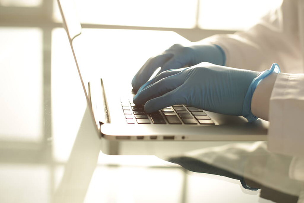 Hastanede mavi eldivenli bir doktor dizüstü bilgisayarda yazıyor. - Fotoğraf, Görsel