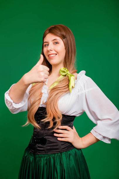Yeşil arka planda saklanmış genç bir kadın el hareketi yapıyor ve gülümsüyor. Aziz Patrick Günü ve Ekim Festivali Kutlama Konsepti. - Fotoğraf, Görsel