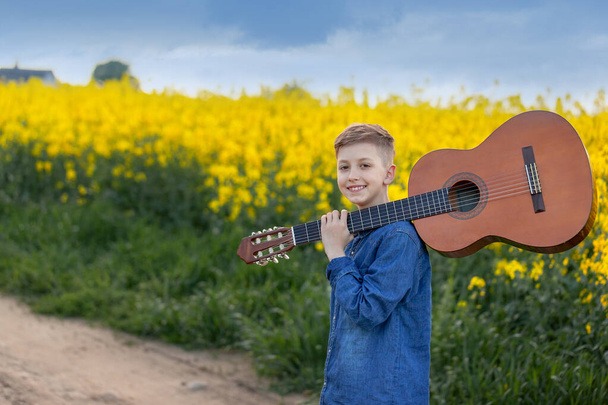 Portrait handsomeboy with guitar walking on the summer road. Young musician on the road to success. - 写真・画像