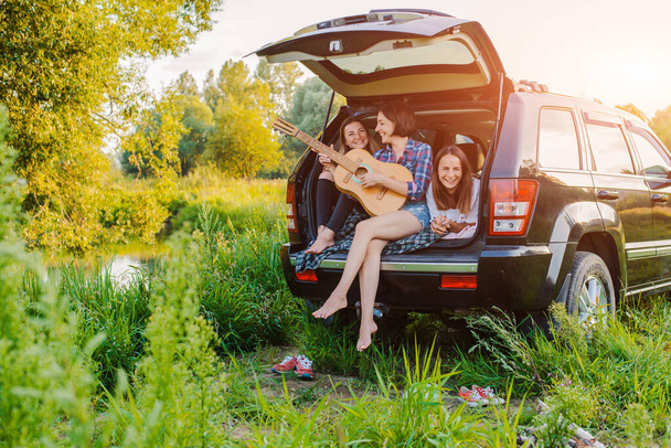Disfrutando del descanso y socializando en un viaje de picnic con tus mejores amigos. Un grupo de mujeres jóvenes y alegres viajan en coche por la naturaleza. Hipster niñas risa al atardecer
. - Foto, imagen