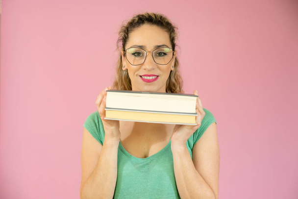 Closeup portrait of beautiful woman with glasses holding books over pink background. - Foto, Imagen