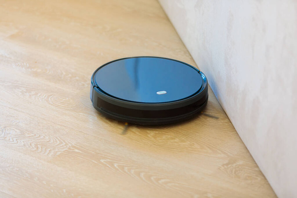 The circular robot vacuum cleaner collects debris from the living room floor. - Photo, image
