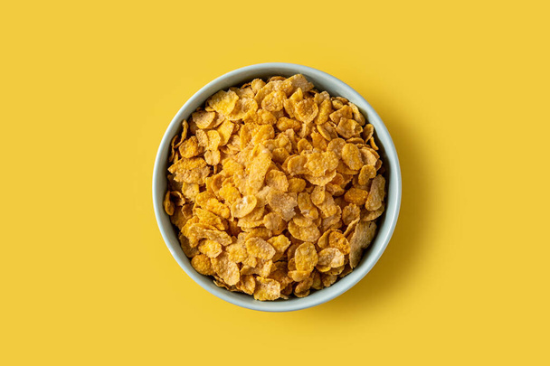 Copos de maíz en un tazón azul sobre fondo amarillo. Vista superior - Foto, imagen
