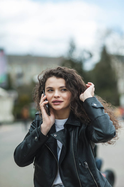 Portrait of attractive curly hairstyle dark skin person speak phone toothy smile free time weekend walking outdoors - Foto, afbeelding