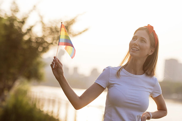 Frau mit Regenbogenfahne im Freien. Lesben feiern allein während der Covid-19 Coronavirus-Pandemie Quarantäne, soziales Distanzierungskonzept - Foto, Bild