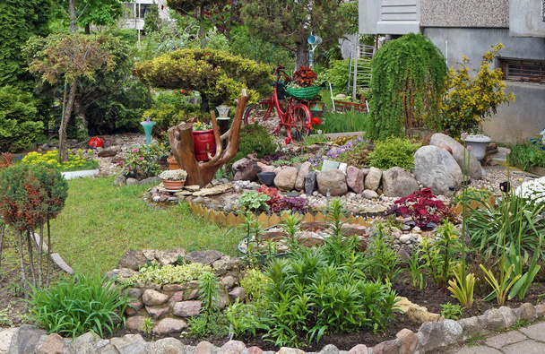 Pieni puutarha ganiittikivillä ja koristepensailla ja kasveilla kaupungin monikerroksisen rakennuksen lähellä  - Valokuva, kuva