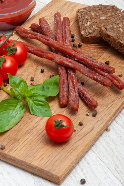 Thin sausages with tomatoes and herbs and black bread on a wooden board - Fotografie, Obrázek
