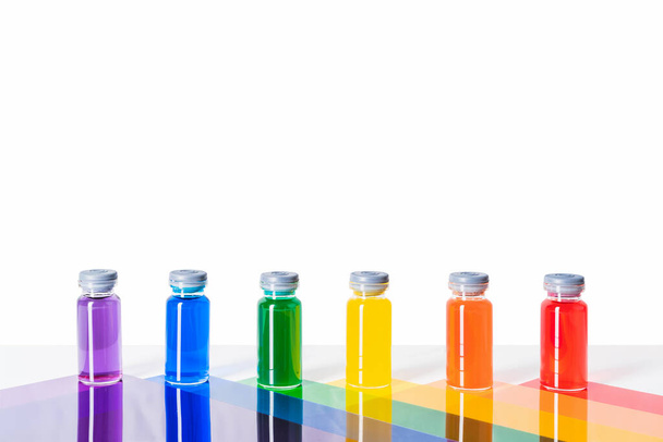 glass vials with rainbow-coloured liquid on multicoloured triangles.Vaccine concept and covid. copy space - Foto, Imagem
