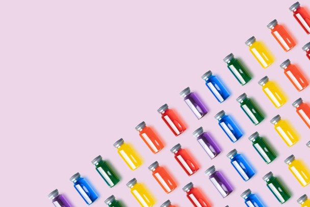 Patroon van glazen flacons met regenboogkleurige vloeistof op roze achtergrond.Vaccin en covid concept. kopieerruimte. - Foto, afbeelding