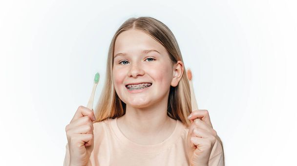 Usmívající se blondýnka dívka s ortodontické rovnátka drží nulový odpad bambusu zubní kartáček - Fotografie, Obrázek