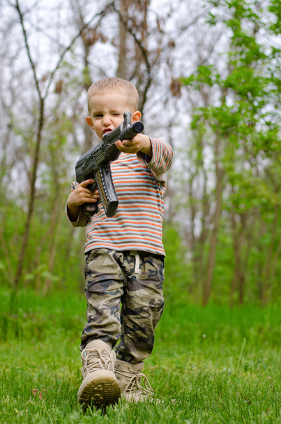 Menino carregando uma metralhadora saudando
 - Foto, Imagem