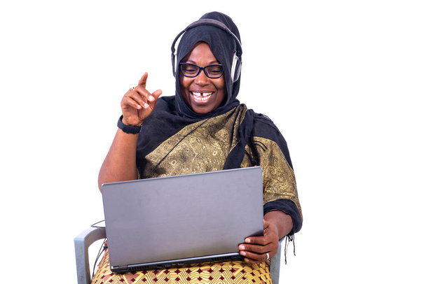 mooie moslim zakenvrouw zitten op witte achtergrond communiceren met behulp van laptop en koptelefoon glimlachen. - Foto, afbeelding