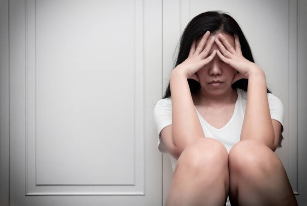 Ασιάτισσα γυναίκα με τα χέρια στο πρόσωπό της, κλαίει ενώ κάθεται στο πάτωμα, αισθάνεται λυπημένη κουρασμένη και υποφέρει από μείζονα καταθλιπτική διαταραχή. Ψυχική υγεία ή ψυχολογική έννοια - Φωτογραφία, εικόνα