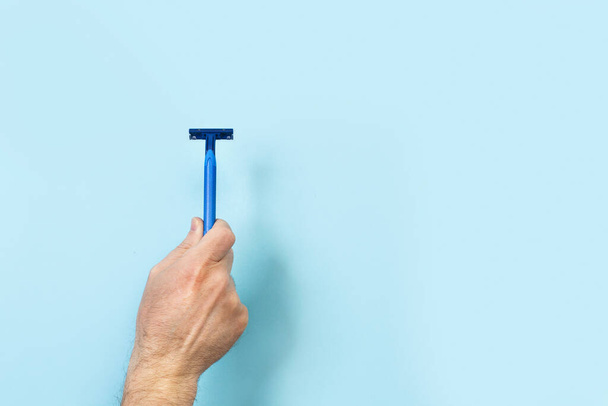 Man hand holding a razor on a blue  background with copy space - Foto, afbeelding