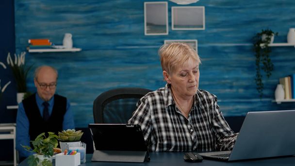 Dizüstü bilgisayarda ve tablette aynı anda birden fazla görev yapan emekli kadın. - Fotoğraf, Görsel