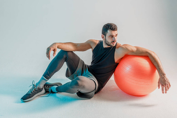フィットネスボール付きの床に座っているスポーツマン - 写真・画像