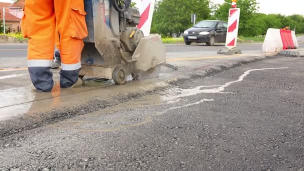 Pracownik używa tarczowej piły diamentowej do precyzyjnego cięcia asfaltu. Wykorzystuje działanie ścierne do przecięcia materiału, gdy piła obraca się z dużą prędkością. - Materiał filmowy, wideo