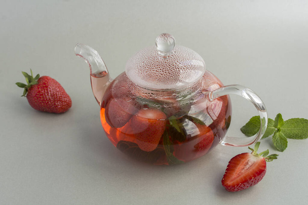 Thé aux fraises dans la théière en verre sur le fond gris. Une boisson saine. Gros plan. - Photo, image