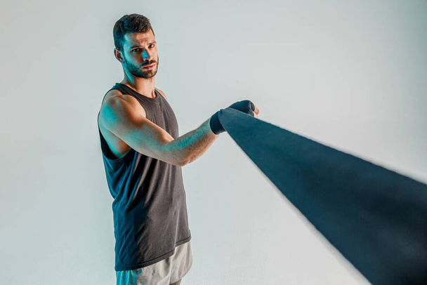 Спортсмен обертывает боксерскую повязку на руку в студии - Фото, изображение