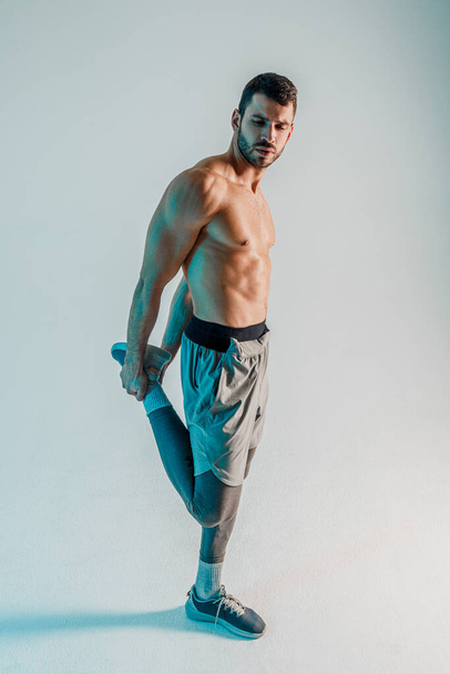 Sportsman stretching leg before training in studio - Fotografie, Obrázek