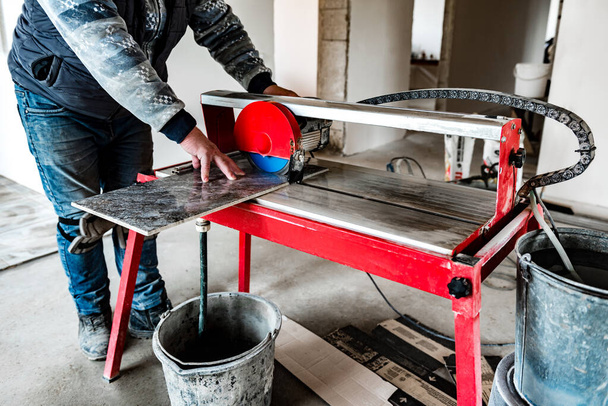 Um trabalhador está cortando uma telha cerâmica em uma máquina de serra de corte molhado. - Foto, Imagem