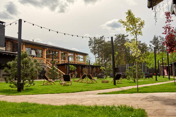 Hölzerner Alkoven-Pavillon im Vorort-Golfclub. Der Ort für die Freizeit Longe, Liegestühle. Kinder auf dem Spielplatz Hüpfen und Springen auf dem Trampolin im Hinterhof - Foto, Bild