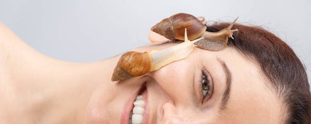 A beautiful caucasian woman is lying on her side and snails are crawling over her face. Skin care and anti-aging - Fotografie, Obrázek