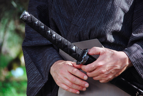 Самурайские руки с типичным мечом, зеленый и дерево на заднем плане - Фото, изображение