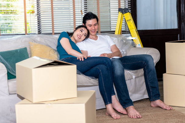Asiatisches junges Paar, Ehemann und attraktive Frau sind glücklich und sitzen auf dem Sofa, nachdem sie es satt haben, in ein neues Zuhause zu ziehen, zu Familienmenschen und Umzugskonzept. - Foto, Bild